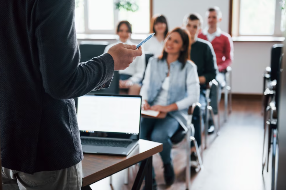 man with pen standing in front of auditory with sitting students