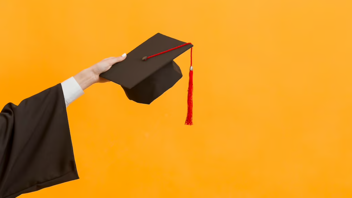 hand holding the master's degree hat and yellow background behind