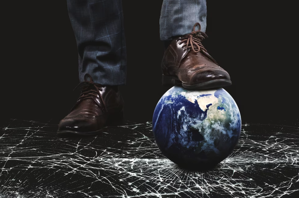 mans legs in brown shoes stands leaning on the globe