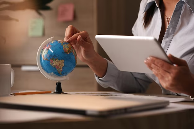 Hand holding a tablet and pointing on a globe with the other hand