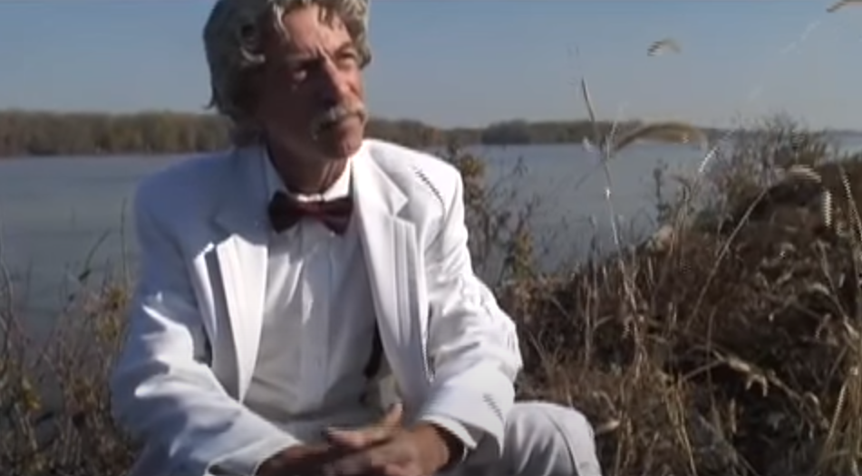 Mark Twain sitting outdoors by the lake amidst grasses